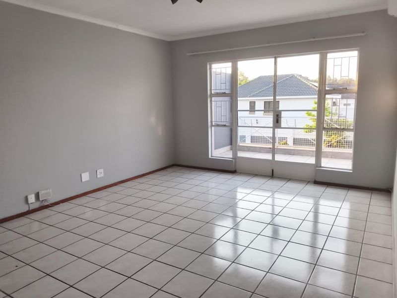 A bright, empty living room featuring neutral grey walls, ceramic tiled flooring, and a large sliding glass door providing access to an outdoor balcony.