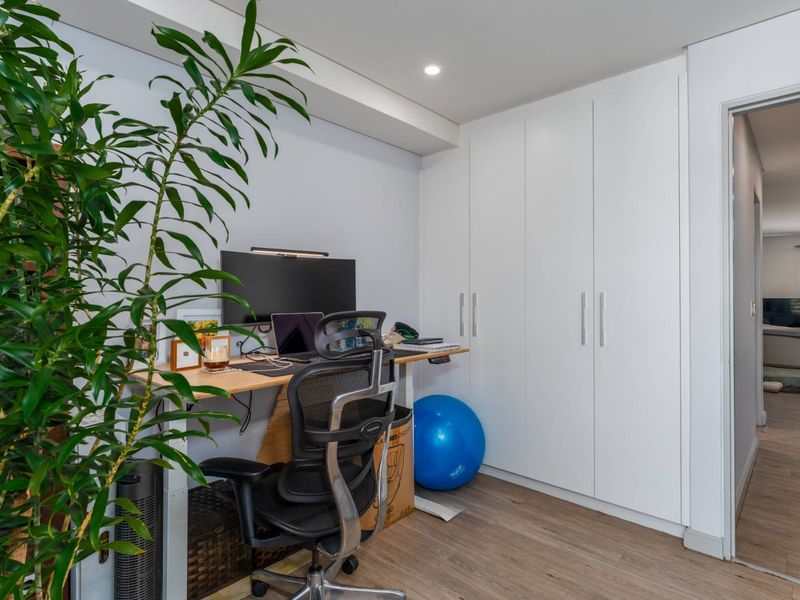 A functional home office space featuring built-in floor-to-ceiling wardrobes, recessed lighting, and modern laminate flooring.