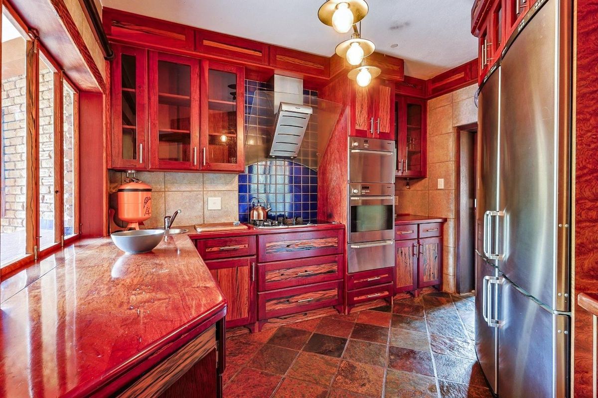 A kitchen featuring custom stained wood cabinetry, stone countertops, built-in stainless steel double ovens, a gas hob with extractor fan, and slate tile flooring.