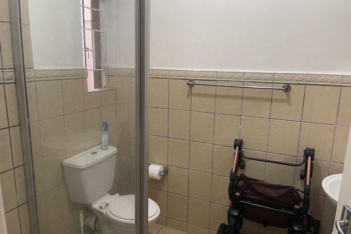 A functional bathroom featuring a glass-enclosed shower, standard toilet, and wall-mounted basin with neutral ceramic tiling.