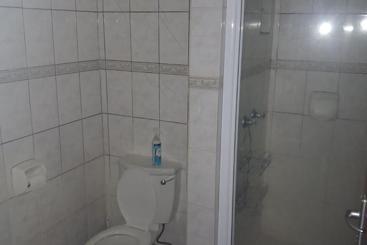 A functional bathroom featuring a white ceramic toilet and a separate glass-enclosed shower stall with tiled walls.