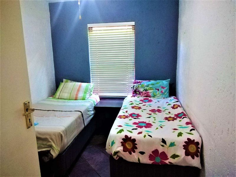 A compact bedroom featuring tiled flooring and a window with venetian blinds, currently configured with two single beds.