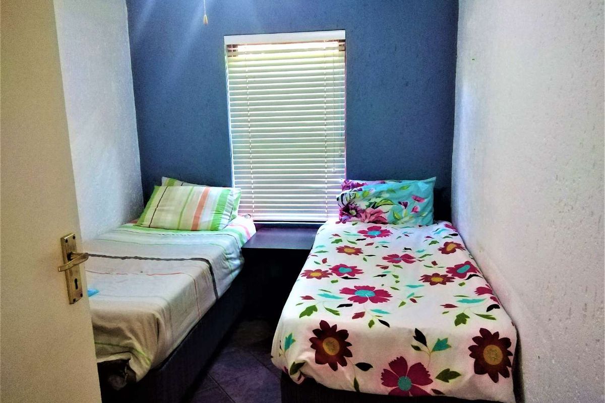 A compact bedroom featuring tiled flooring and a window with venetian blinds, currently configured with two single beds.