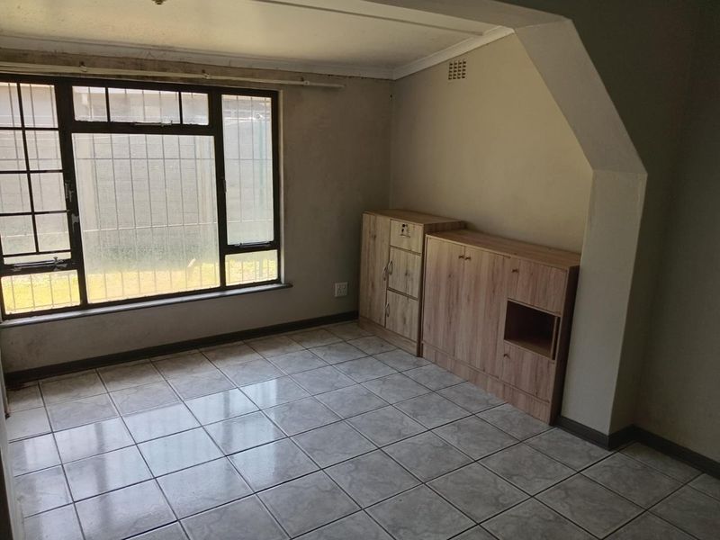 An empty living area featuring tiled flooring, an archway, and a large window with security bars, requiring cosmetic updates to improve its overall condition.