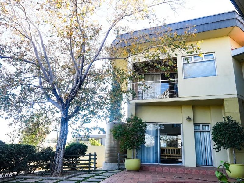 Rear view of a two-story house featuring a paved patio, a balcony with metal railings, and a large water tank in the garden.