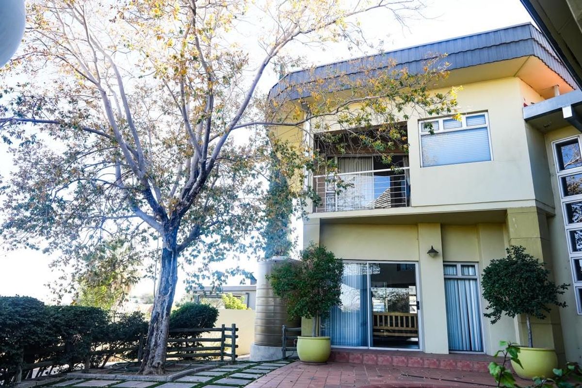 Rear view of a two-story house featuring a paved patio, a balcony with metal railings, and a large water tank in the garden.
