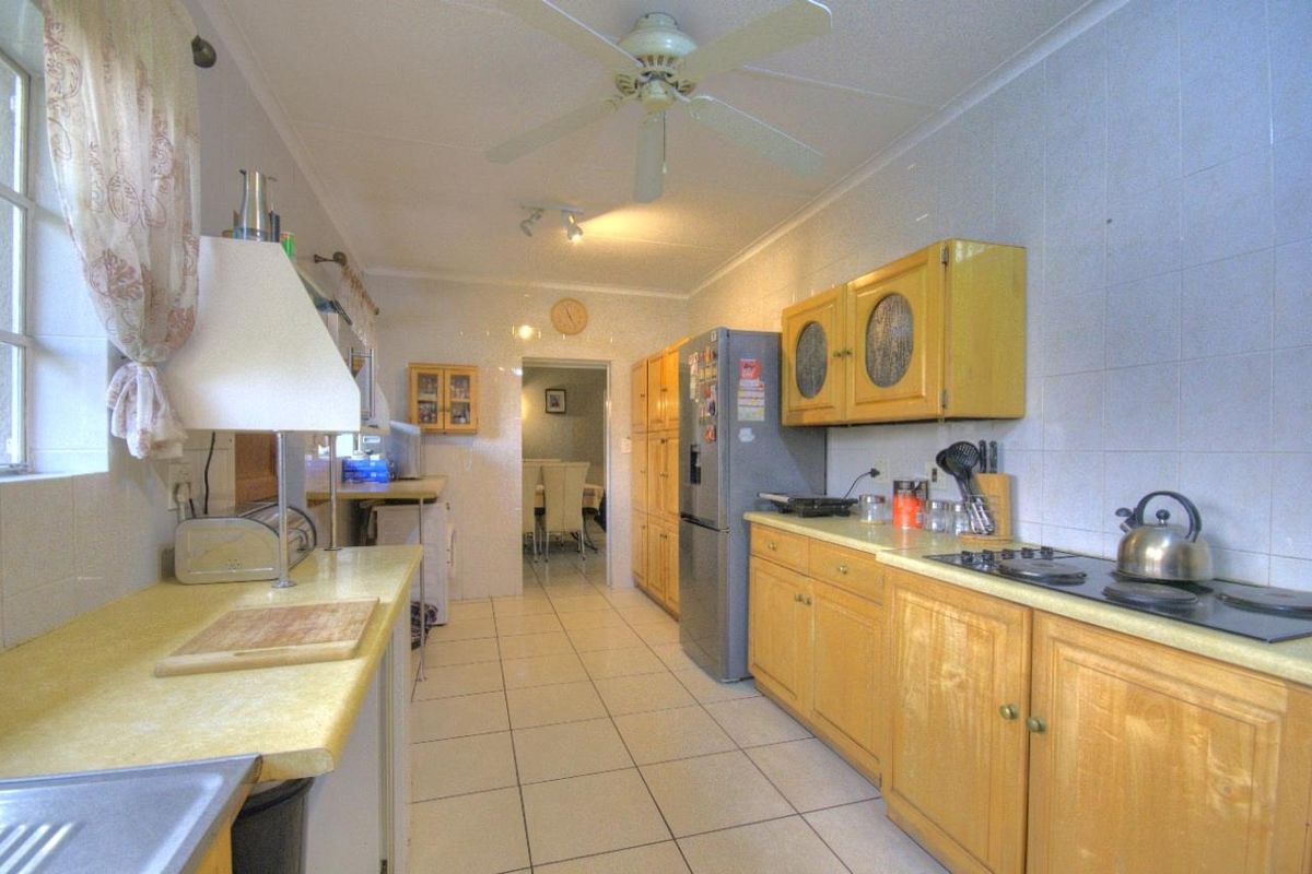 A functional galley-style kitchen featuring wooden cabinetry, tiled flooring, and integrated cooktop, offering a traditional layout with direct access to the dining area.