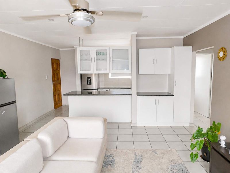 Open-plan living area featuring a modern kitchen with white cabinetry, granite countertops, and tiled flooring throughout.