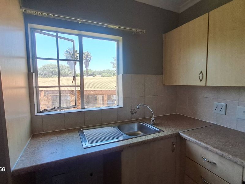 A functional kitchen featuring laminate cabinetry, tiled backsplash, and a stainless steel sink with a view of the exterior.