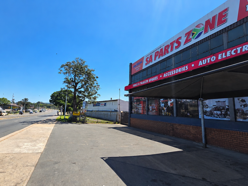 Front exterior view of an industrial commercial property featuring a paved driveway, metal awning, and prominent signage along a main road.
