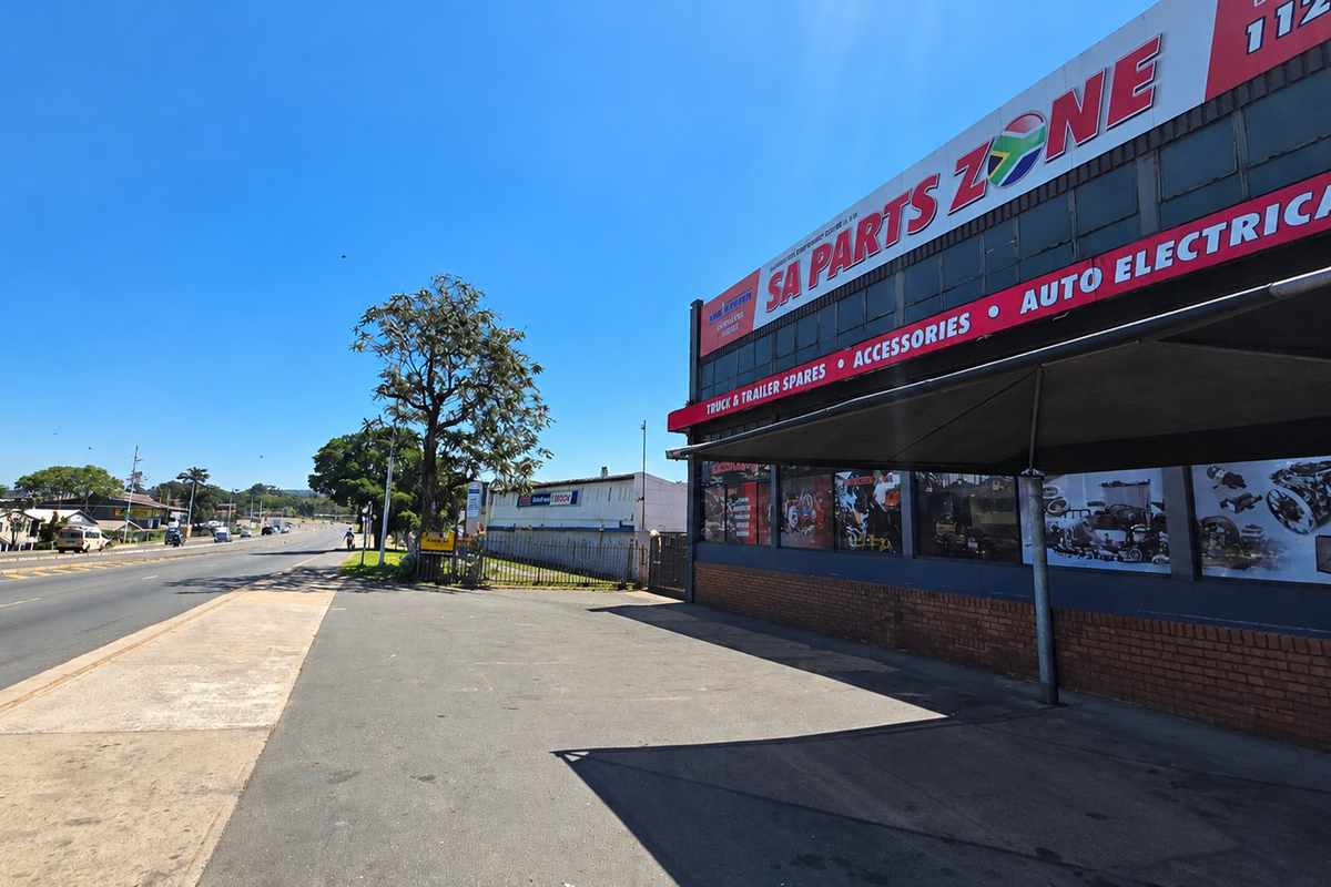 Front exterior view of an industrial commercial property featuring a paved driveway, metal awning, and prominent signage along a main road.