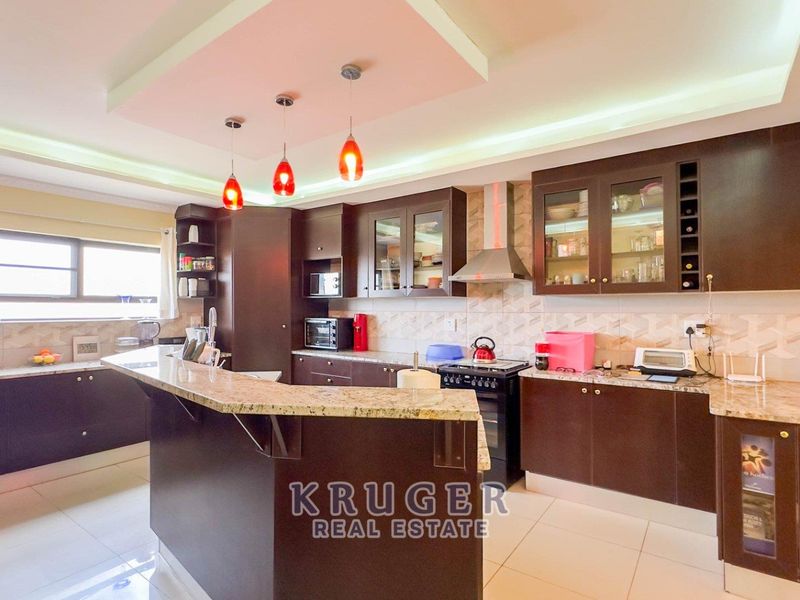 A well-appointed kitchen featuring dark cabinetry, granite countertops, a breakfast bar, and modern recessed lighting with pendant fixtures.