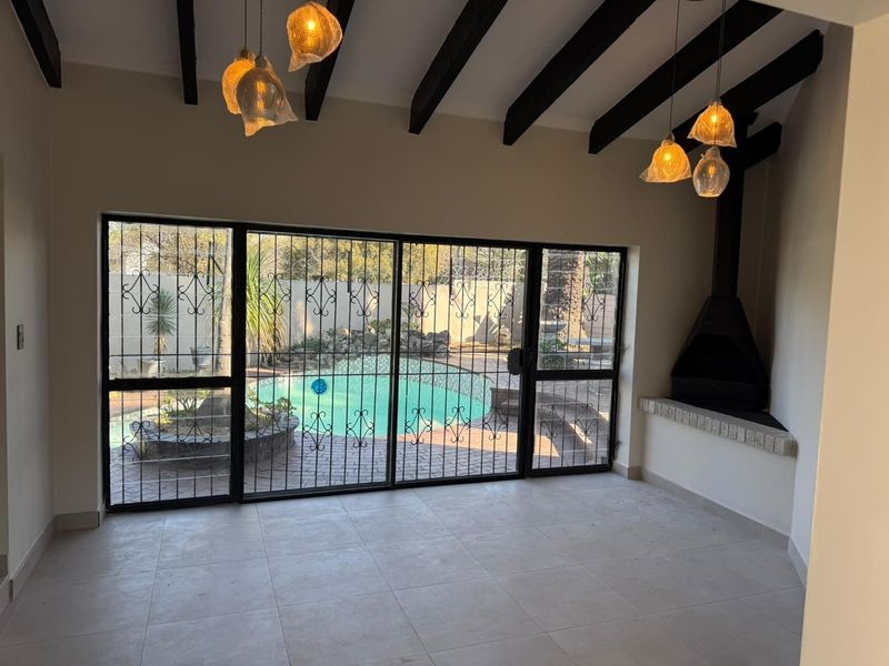 Spacious living area featuring exposed timber ceiling beams, a built-in fireplace, and large sliding doors providing direct access to the pool area.