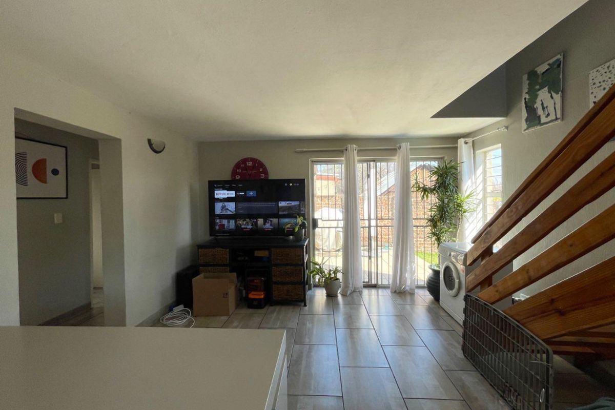 Open-plan living area featuring tiled flooring, a wooden staircase, and sliding glass doors providing access to the rear exterior.