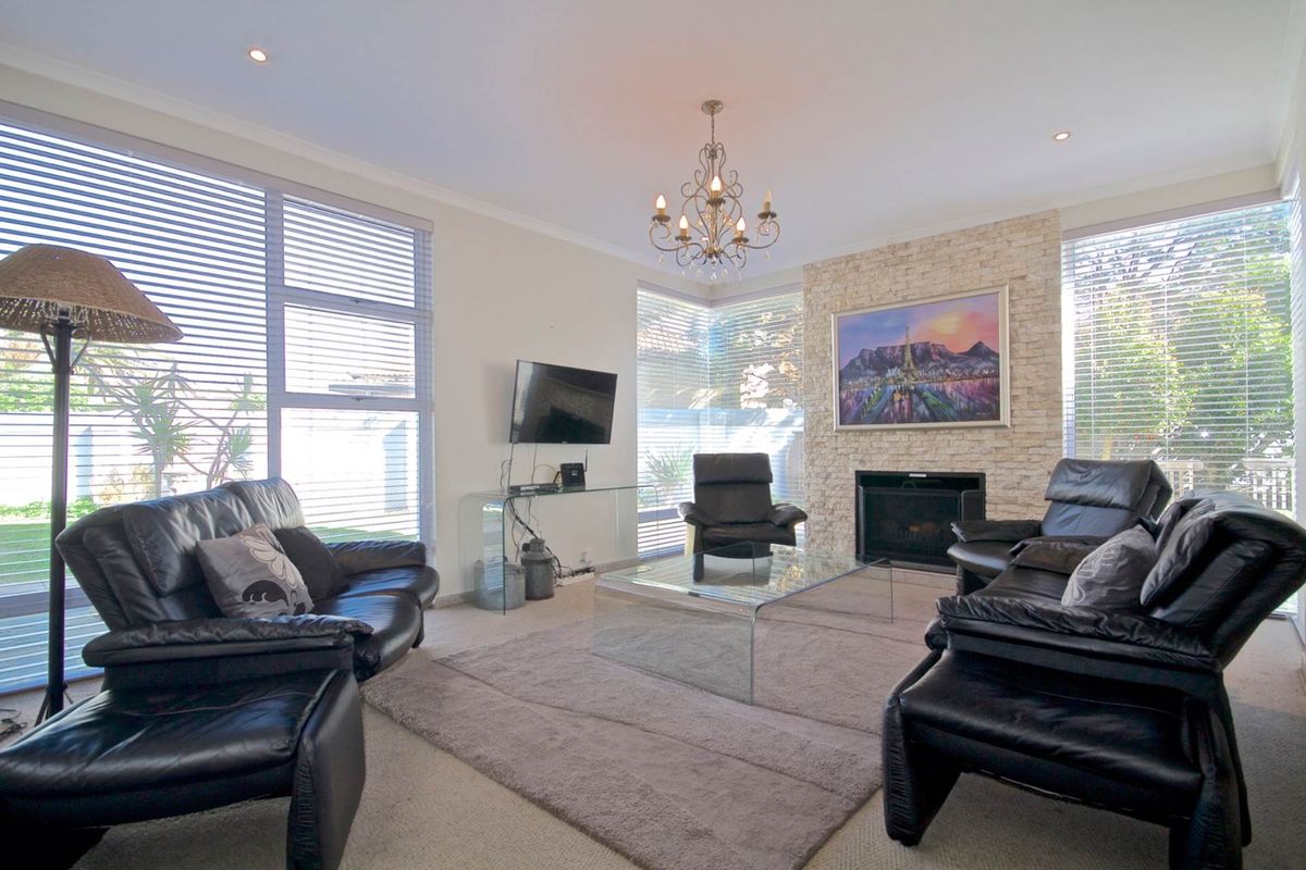 Spacious living room featuring a stone-clad fireplace, large windows with venetian blinds, and elegant chandelier lighting.