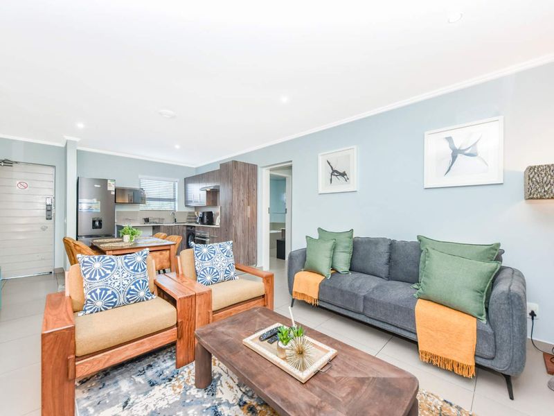 A bright open-plan living and kitchen area featuring modern cabinetry, tiled flooring, and recessed lighting, creating a functional and inviting space.