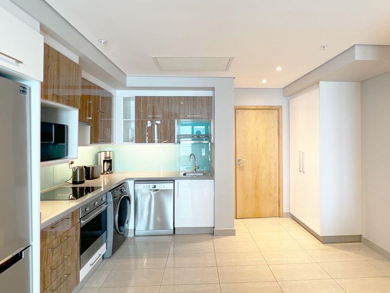 Modern kitchen featuring sleek wood-grain and white cabinetry, integrated appliances, stone countertops, and tiled flooring in an open-plan layout.