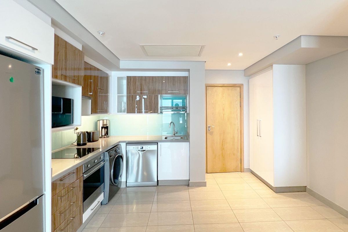 Modern kitchen featuring sleek wood-grain and white cabinetry, integrated appliances, stone countertops, and tiled flooring in an open-plan layout.