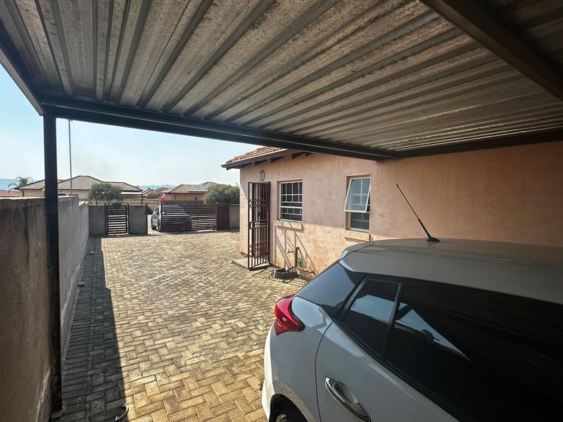 A covered carport area featuring a corrugated metal roof, paved driveway, and secure perimeter walling with gated access.