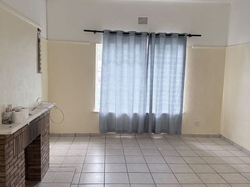 An empty living room featuring a brick fireplace, tiled flooring, and neutral wall finishes, offering a blank canvas for potential renovation or staging.