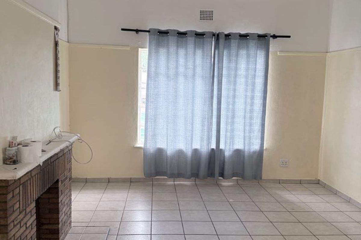 An empty living room featuring a brick fireplace, tiled flooring, and neutral wall finishes, offering a blank canvas for potential renovation or staging.