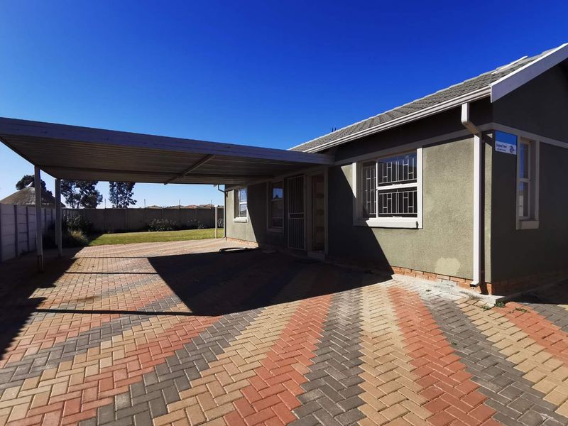 Front exterior view of the house featuring a paved driveway, a covered carport, and secure window bars.