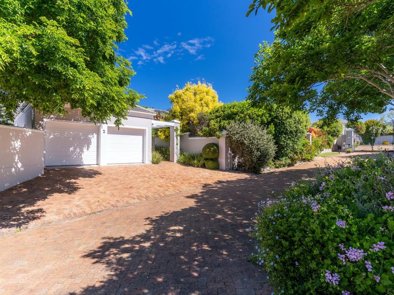 A well-maintained front exterior featuring a double garage, paved driveway, and established garden with mature trees and boundary walls.