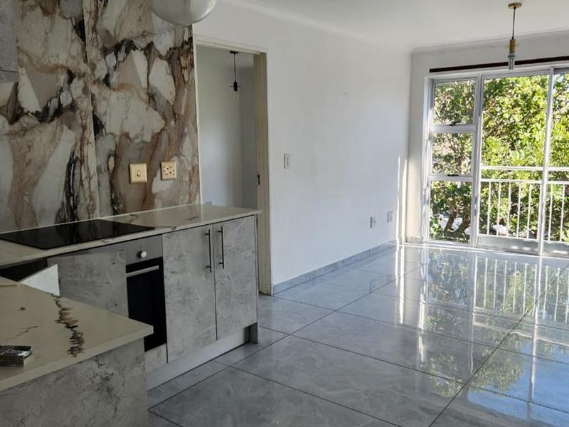 Modern open-plan kitchen and living area featuring marble-effect finishes, sleek porcelain tiling, and large sliding doors leading to a balcony.