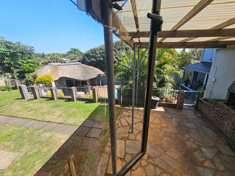 Covered patio area with flagstone paving and built-in braai, overlooking a garden with a swimming pool and a separate thatched lapa.