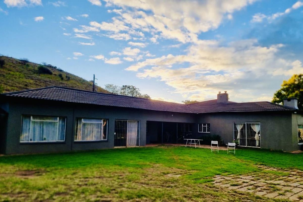 Rear view of a single-story farmhouse featuring a tiled roof, large windows, and a covered patio area overlooking a spacious garden.