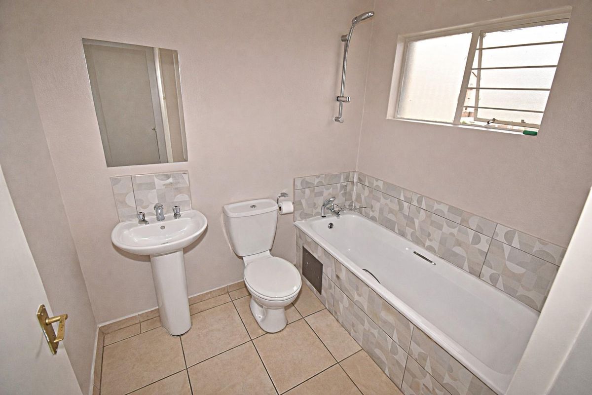 A functional bathroom featuring a pedestal basin, toilet, and a bathtub with a wall-mounted shower head and patterned tile splashbacks.