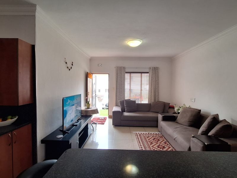 Open-plan living area featuring a kitchen with granite countertops and tiled flooring, seamlessly flowing into a comfortable lounge space with natural light.