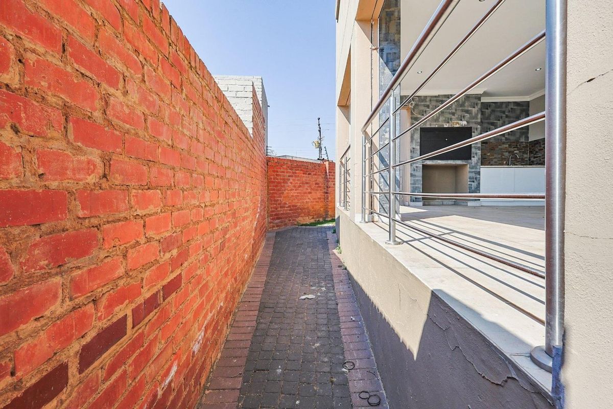 A side walkway featuring a paved path between a brick boundary wall and the raised patio area of the main house.