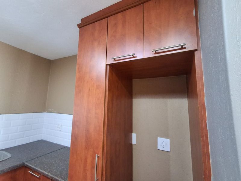 A kitchen area featuring built-in wooden cabinetry, a dark laminate countertop, and a white subway tile backsplash with unfinished wall sections.