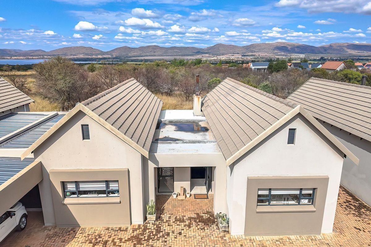 Aerial view of a residential property featuring a tiled roof, paved driveway, and scenic landscape views in the background.