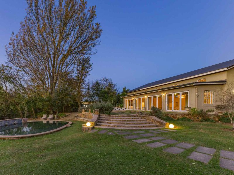 Rear exterior view of the guest house featuring a swimming pool, stone landscaping, and multiple glass sliding doors leading to the garden.
