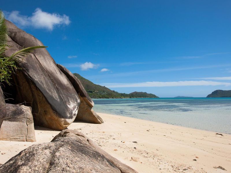 A scenic view of a pristine sandy beach with large granite boulders and clear turquoise ocean waters.