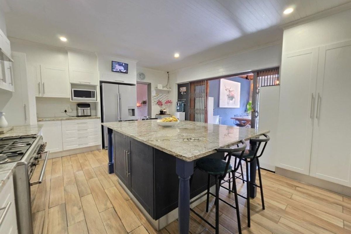 Modern kitchen featuring a large central island with granite countertops, gas range, built-in microwave, and shaker-style cabinetry, seamlessly flowing into an outdoor patio area.