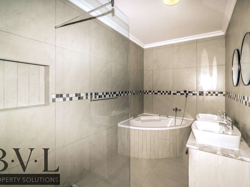 Modern bathroom featuring a corner bathtub, glass shower screen, and a double vanity with contemporary fixtures and neutral tiled finishes.