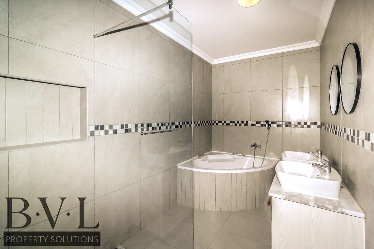 Modern bathroom featuring a corner bathtub, glass shower screen, and a double vanity with contemporary fixtures and neutral tiled finishes.