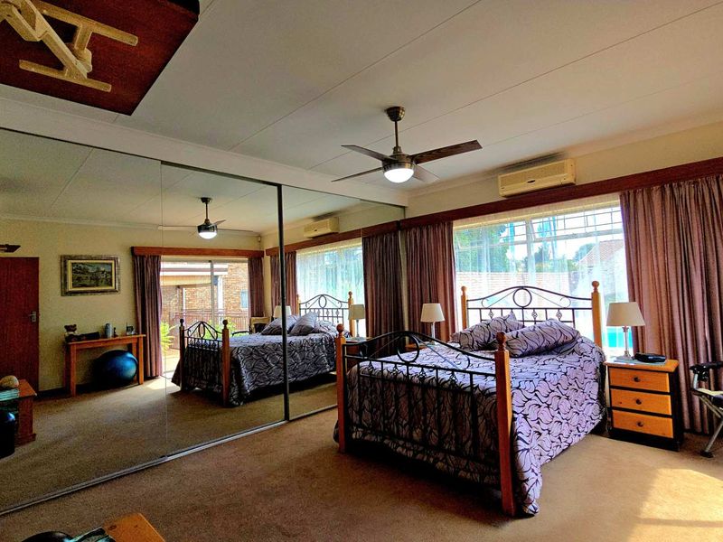 Spacious bedroom featuring large mirrored built-in cupboards, a ceiling fan, and a wall-mounted air conditioning unit.