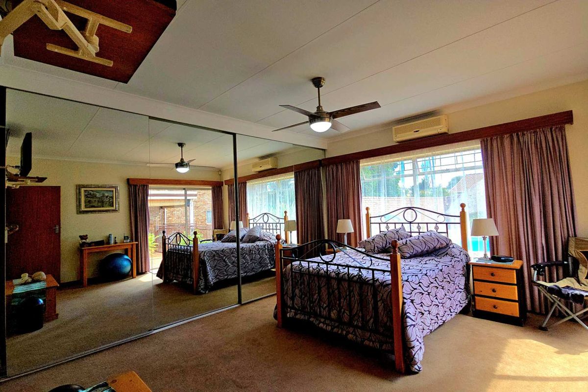 Spacious bedroom featuring large mirrored built-in cupboards, a ceiling fan, and a wall-mounted air conditioning unit.
