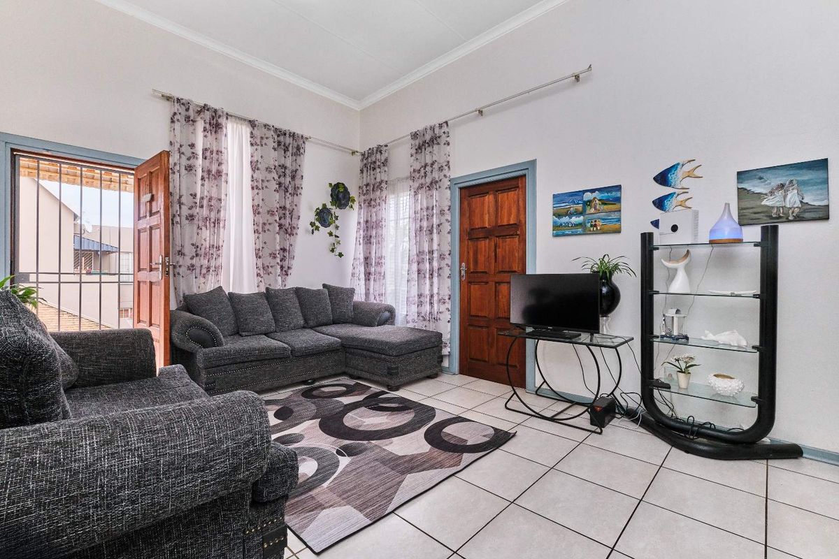 A bright living room featuring tiled flooring, wooden door frames, and direct access to an outdoor area through a security-gated door.