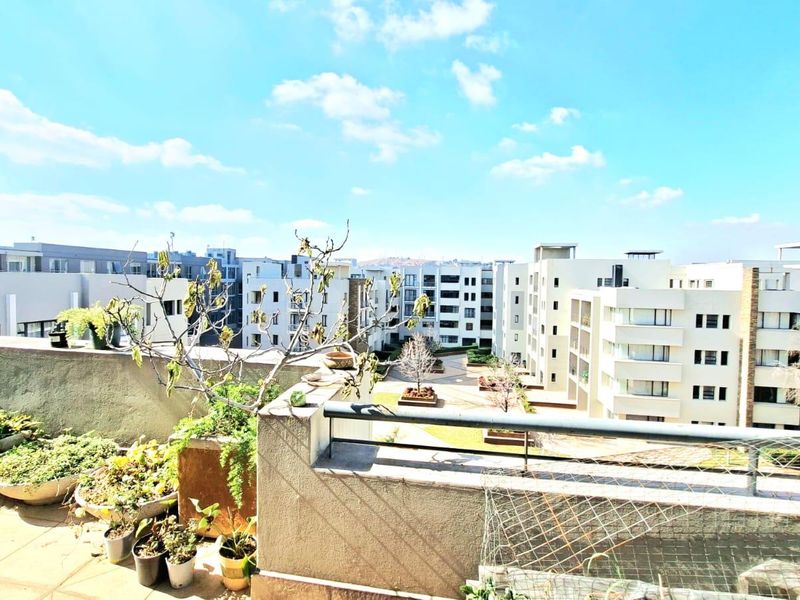 A spacious balcony overlooking the apartment complex courtyard, featuring tiled flooring and metal safety railings.