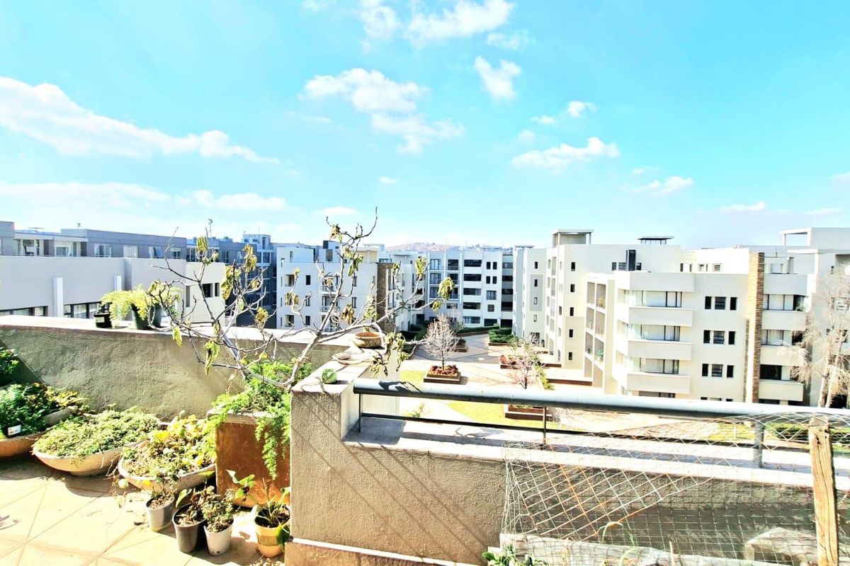 A spacious balcony overlooking the apartment complex courtyard, featuring tiled flooring and metal safety railings.