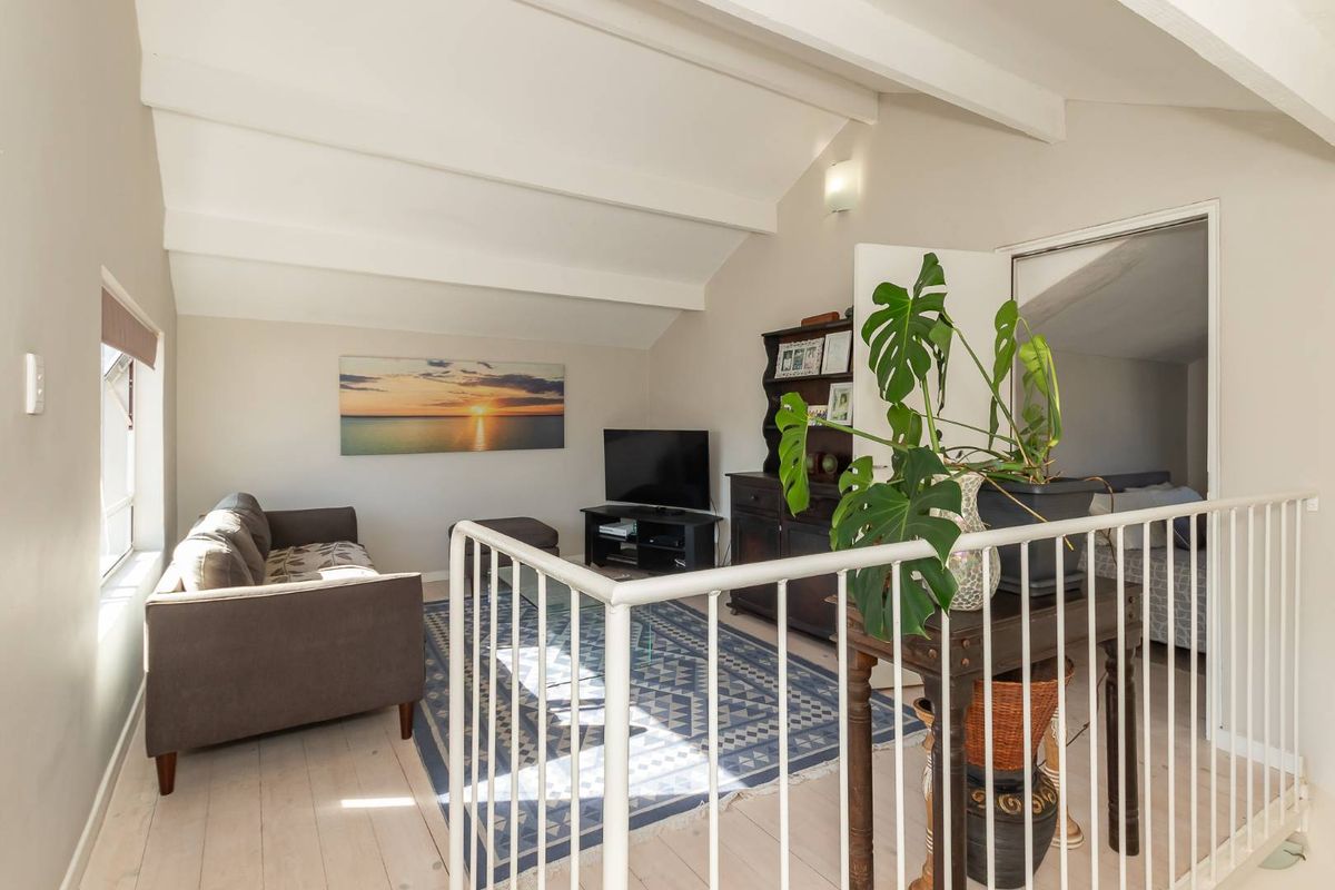 A cozy living area featuring vaulted ceilings with exposed beams and a white metal balustrade overlooking the space.