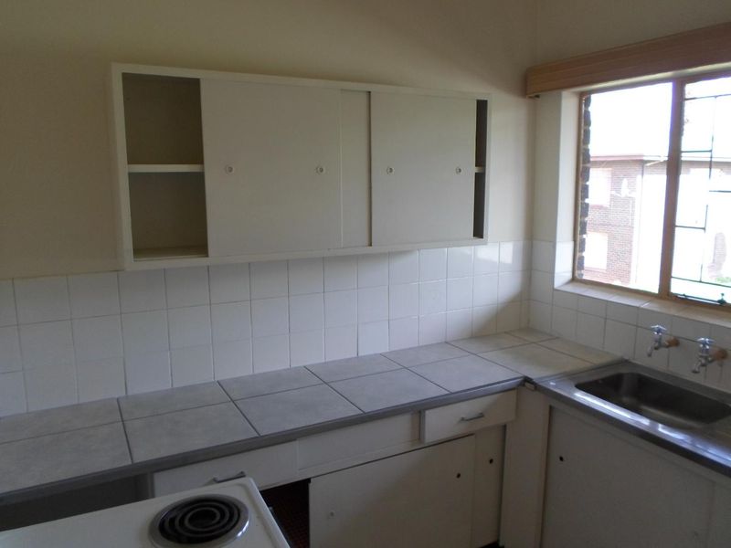 A dated kitchen featuring tiled countertops, a stainless steel sink, and built-in cabinetry, offering a functional space ready for modernization.