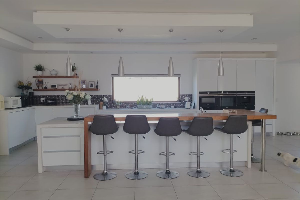 Modern kitchen featuring a large island with breakfast bar seating, integrated appliances, sleek white cabinetry, and a stylish mosaic tile backsplash.