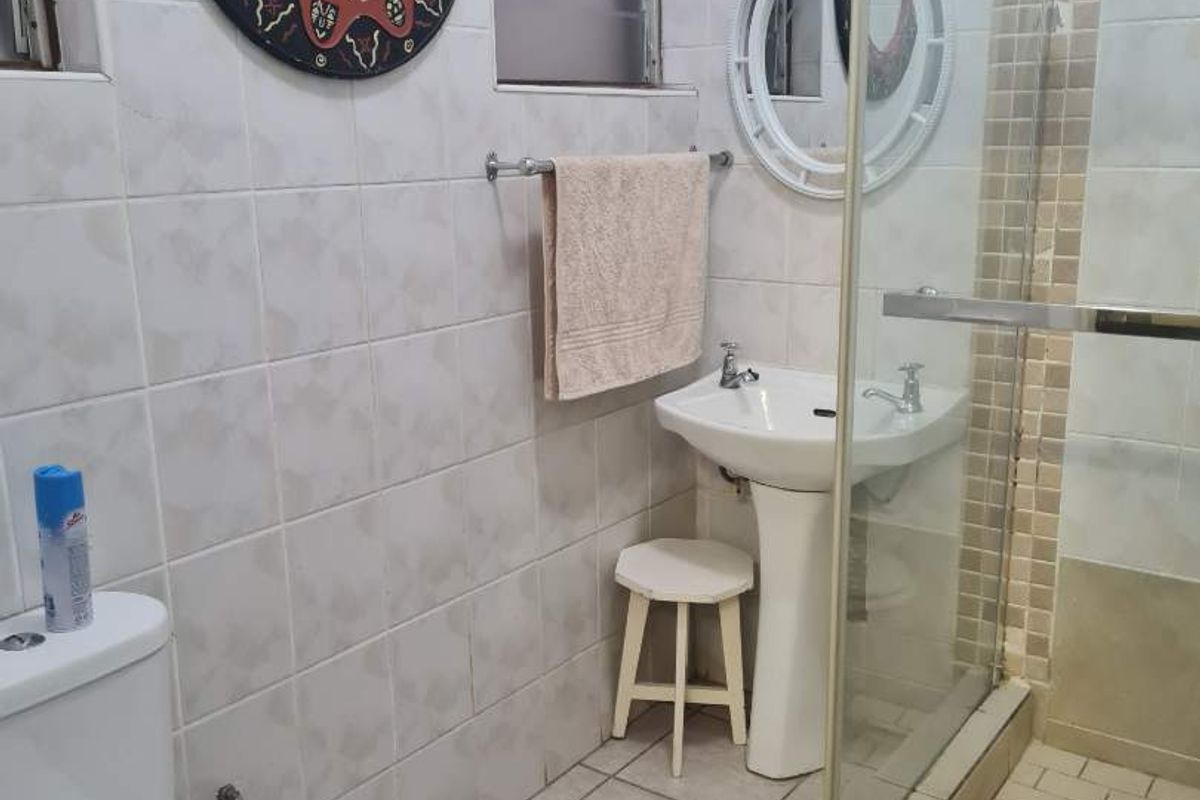 A functional bathroom featuring a pedestal sink, a glass-enclosed shower, and tiled walls and flooring.