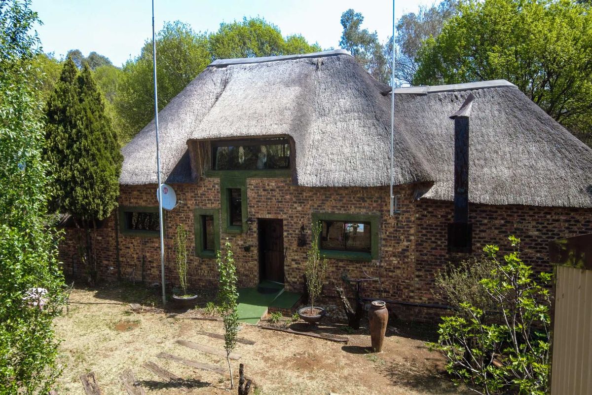 A rustic guest house exterior featuring traditional thatch roofing, exposed brick facade, and a natural garden setting.
